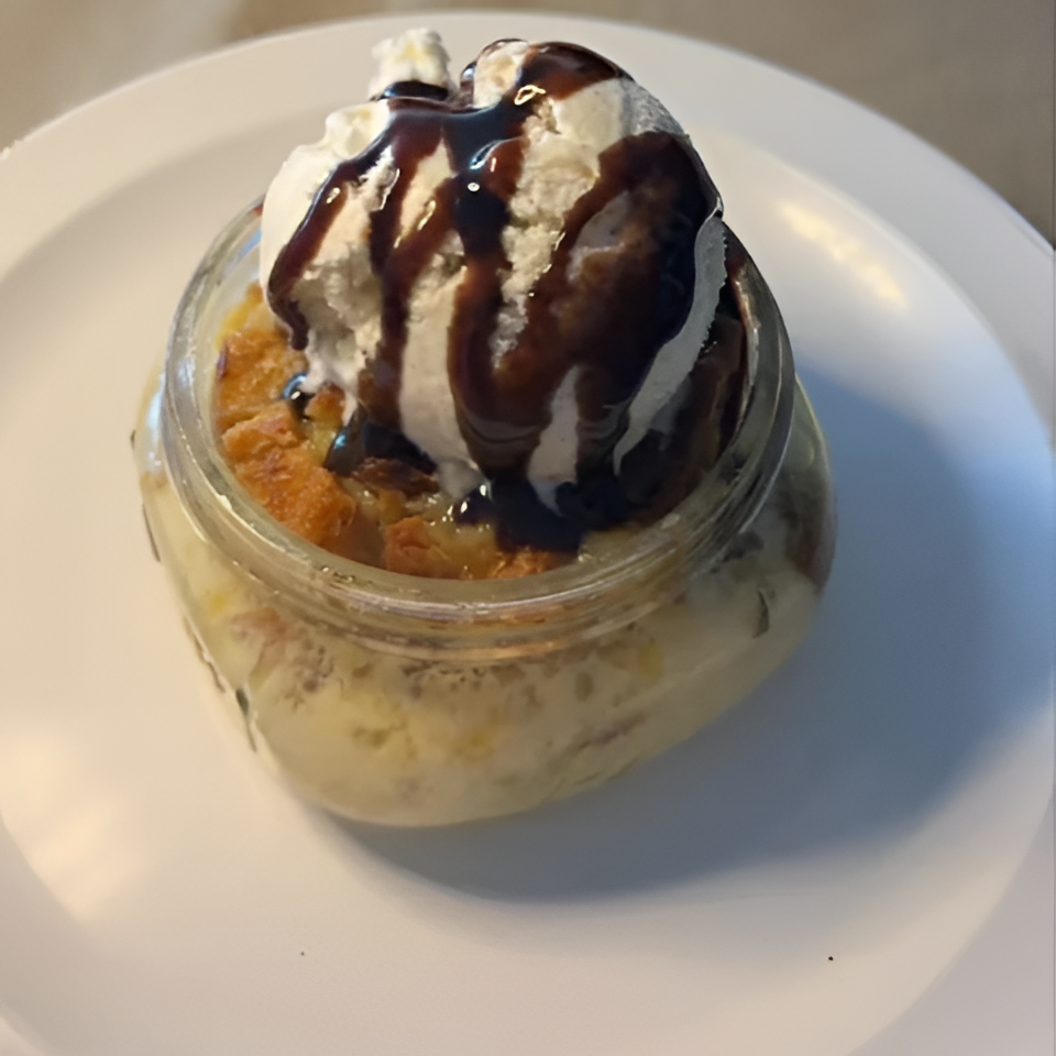 Layered dessert in a glass jar topped with whipped cream and chocolate sauce, served on a white plate.