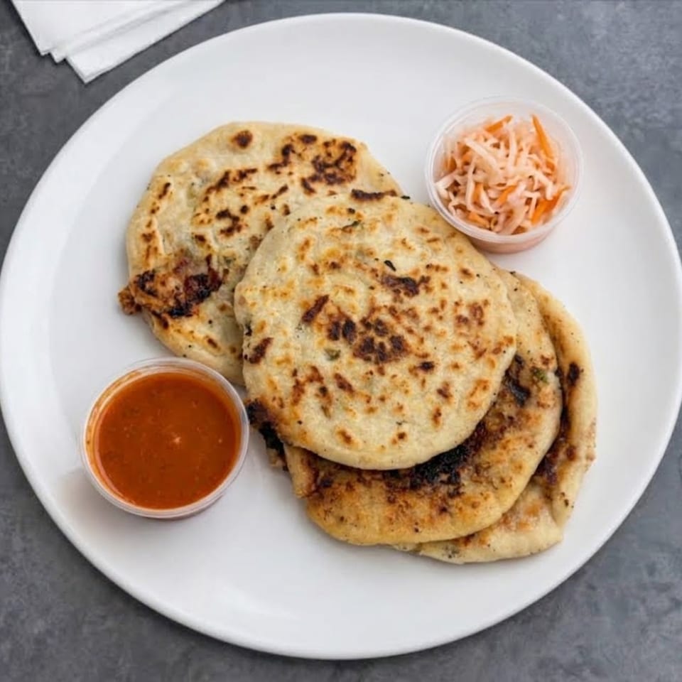 Plate of grilled stuffed flatbreads served with red dipping sauce and a side of shredded carrot slaw.